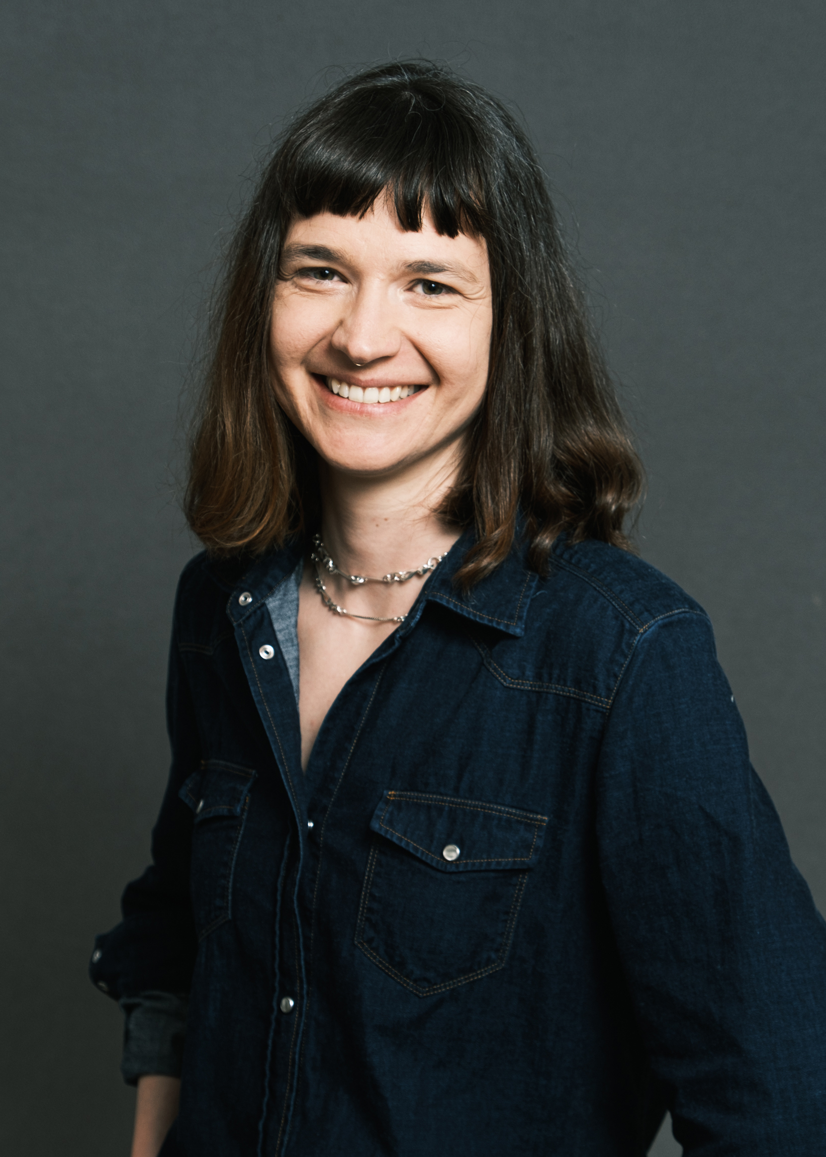 Portrait en studio de Juliette Angotti, praticienne en hypnose Ericksonienne à Marseille et en ligne. Juliette Angotti porte une veste en jeans bleue et sourit à la caméra pour se présenter sur la page d'accueil de son site internet.